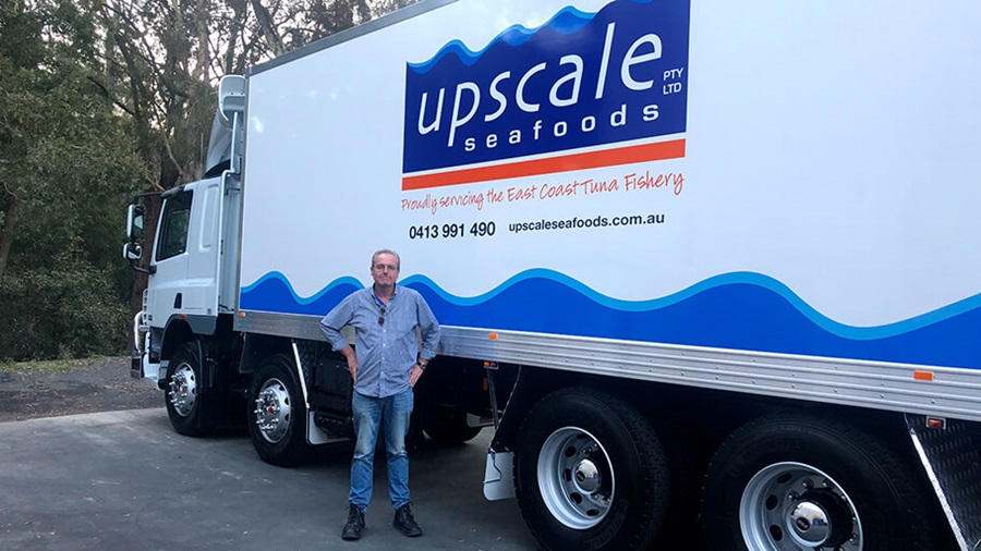 A man standing in front of a large truck with the words 'Upscale Seafoods Pty Ltd: proudly servicing the East Coast Tuna Fishery'