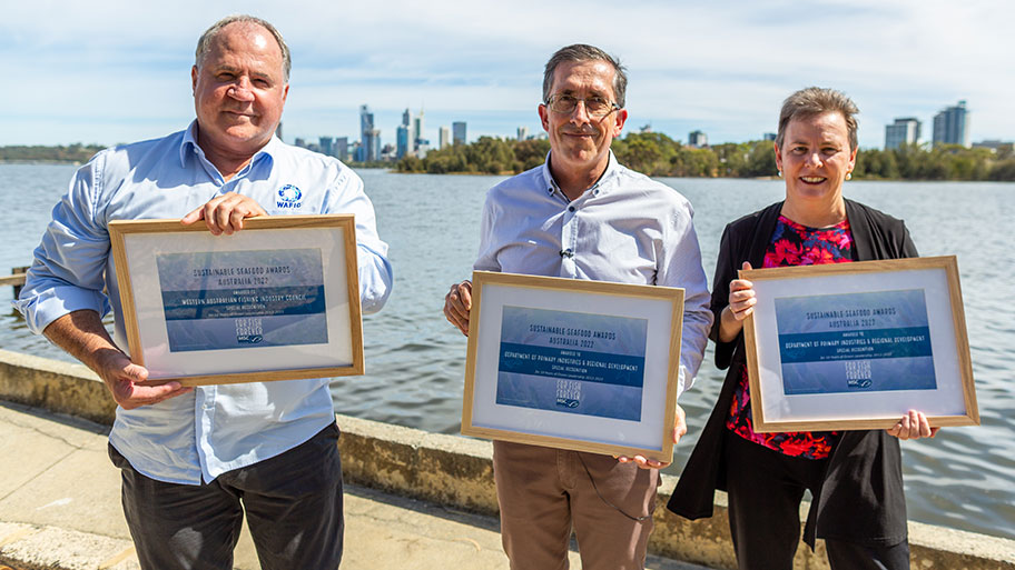 Three people hold award certificates with the Perth skyline behind them