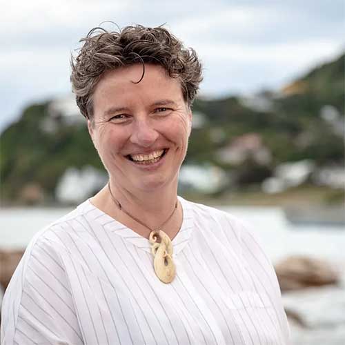 Woman with short hair wearing white pinstripe shirt and Maori bone pendant