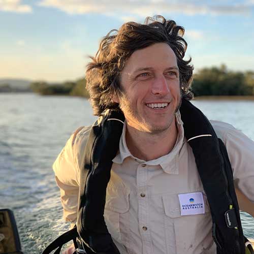 Man on small boat wearing tan shirt and black life jacket