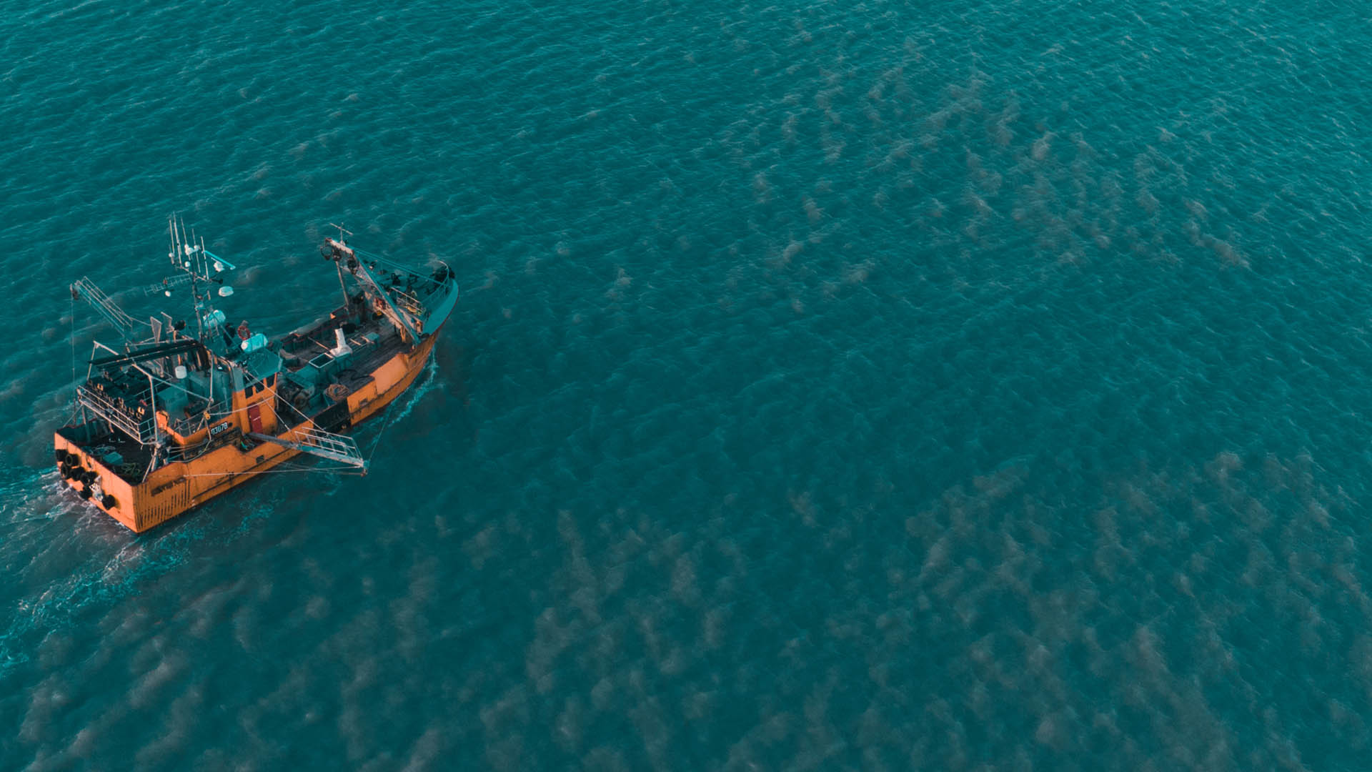 Aerial shot of orange trawler vessel on turquoise water