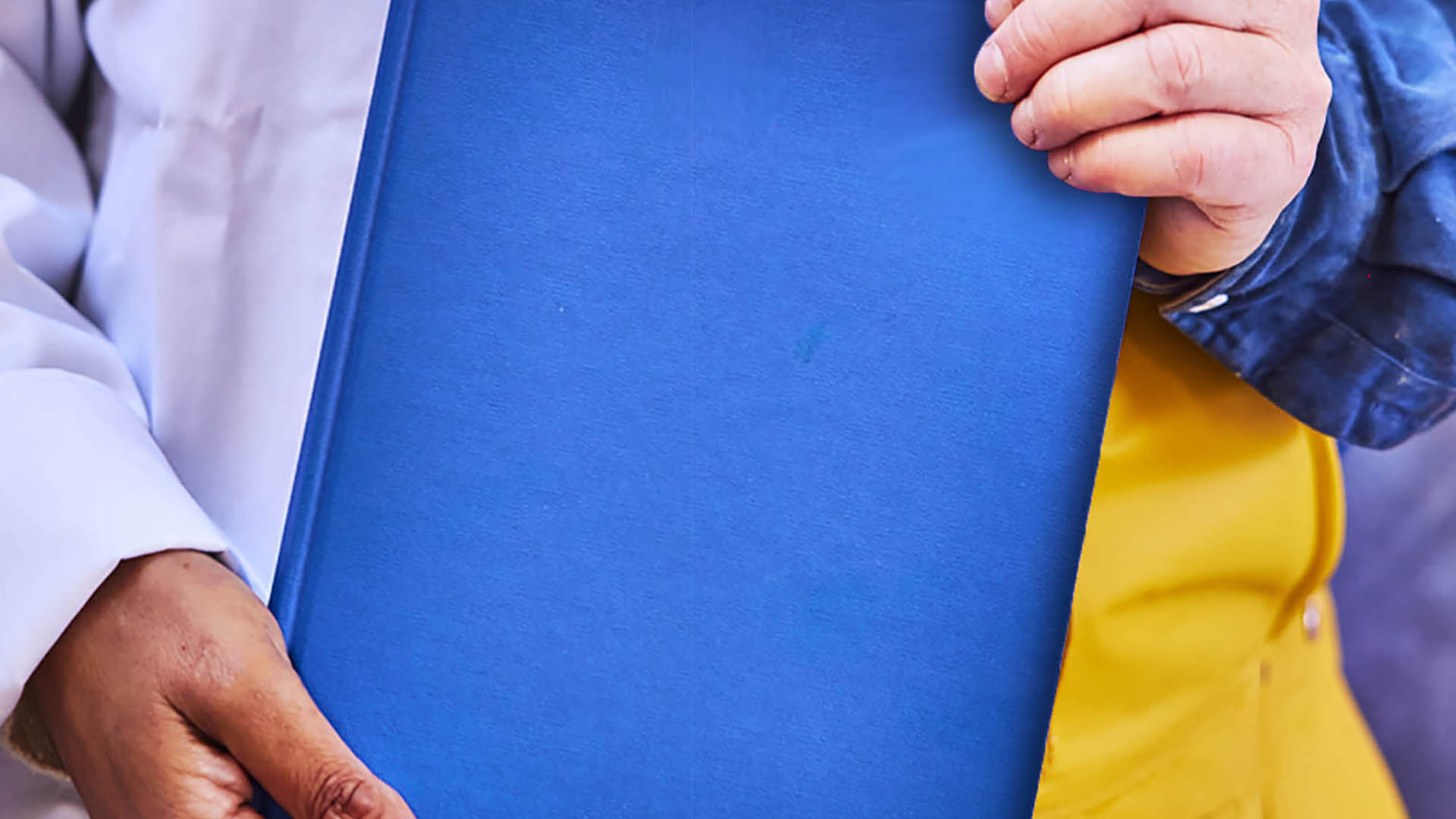 Blue book held at corners by two different hands - one in chef's apron, one in fisher's overalls