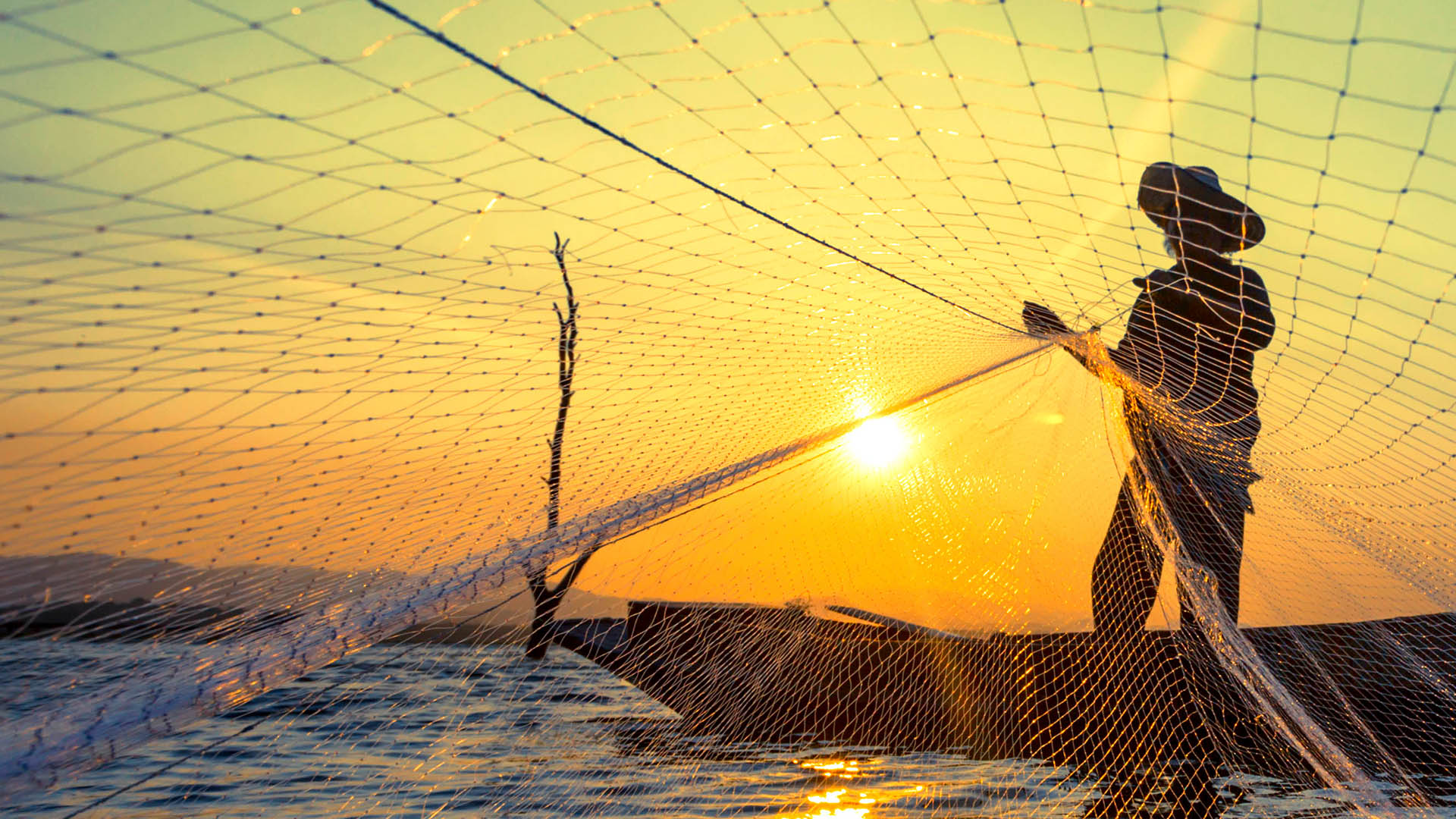 Fisherman throwing a net with the sunset behind him