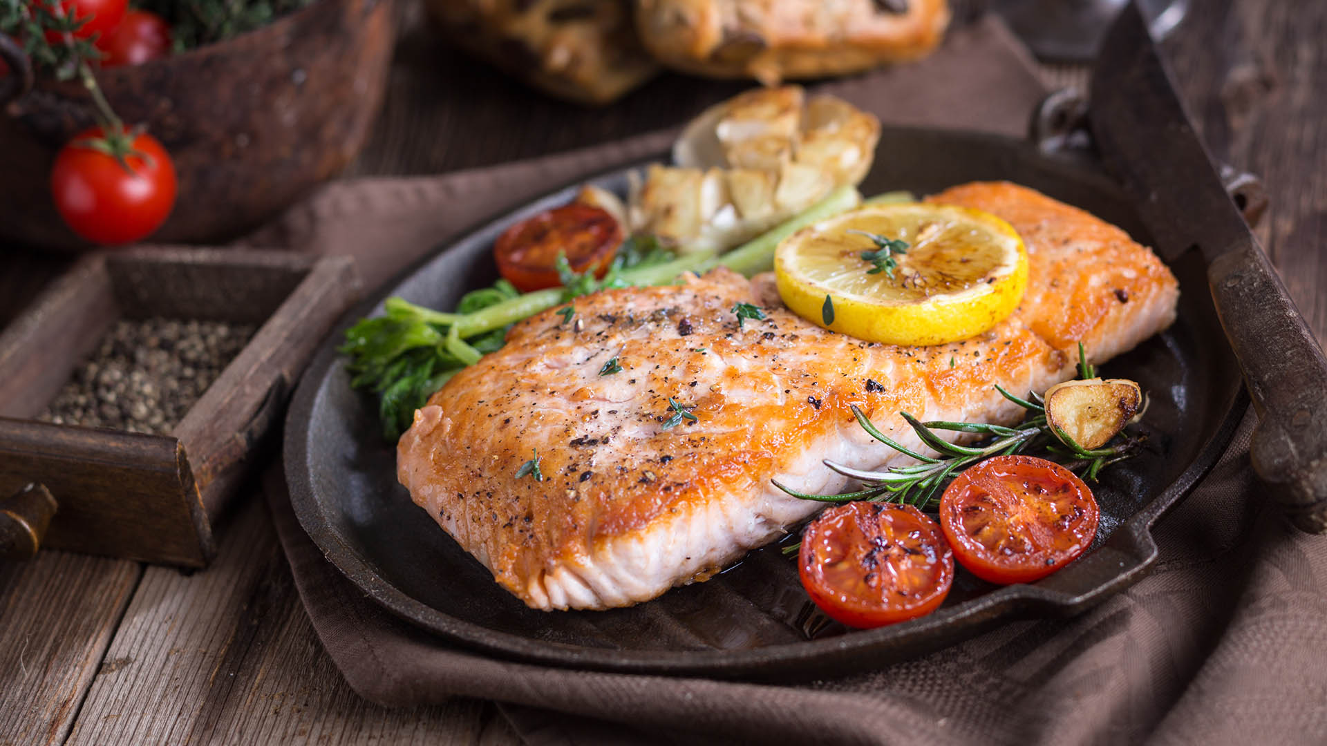 Grilled salmon on metal dish with slice of lemon and tomatoes