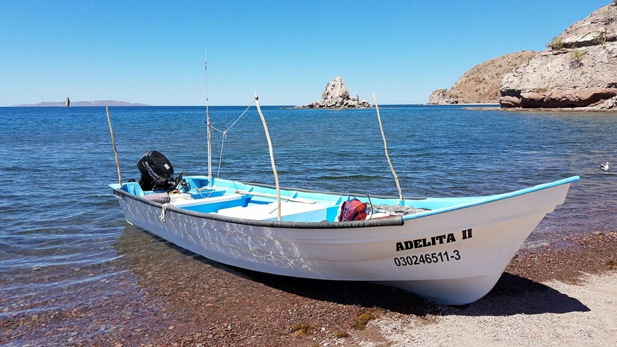 A small fishing boat sitting on the shore with rocks and water in background