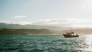 Octopus fishing vessel at sea with mountains and sunshine