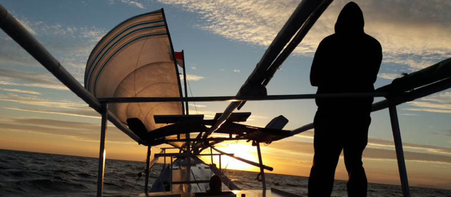 Silhouette of man in hoodie on boat at sunset 