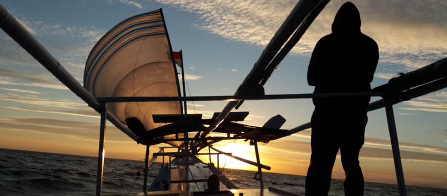 Silhouette of man in hoodie on boat at sunset