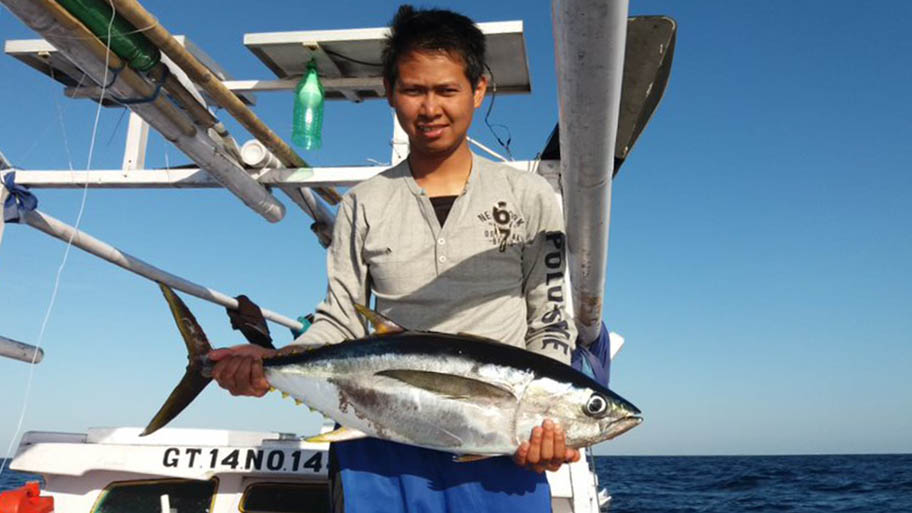 Young man holding large tuna aboard boat