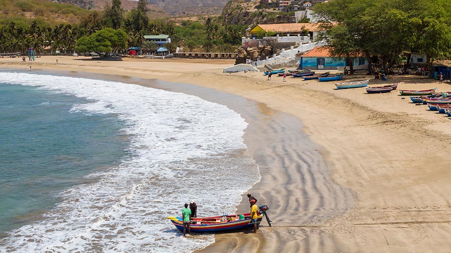 Four people on small wooden boat on a beach at the water's edge