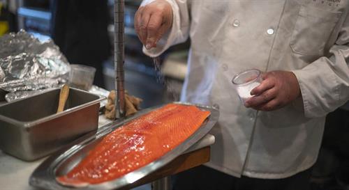 White coated chef sprinkling salt on salmon fillet