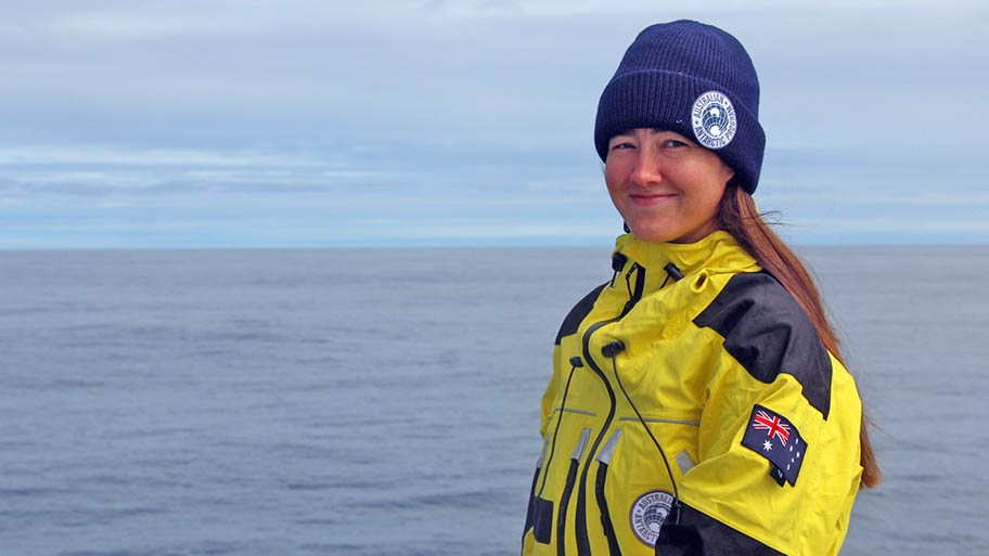 Woman in hat and waterproof jacket with blue sea and sky behind