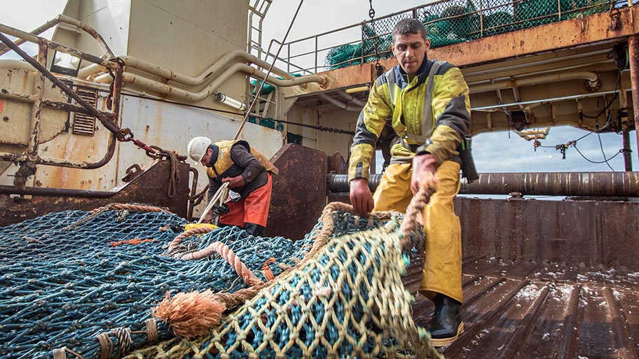 Two men on deck of large fishing vessel, hauling nets