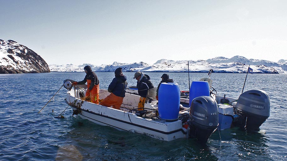 Four fishers on small powered boat with snowy hills behind