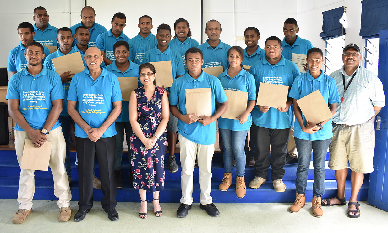 A group of students from Fiji National University in blue shirts standing in two rows holding certificates