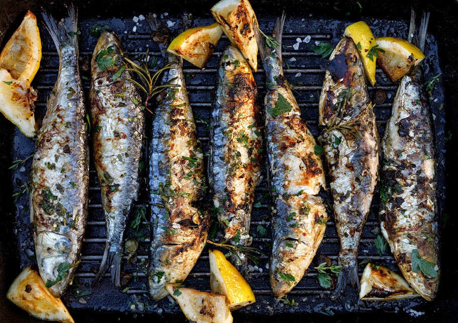 Grilled sardines with lemon pieces on a grill plate.