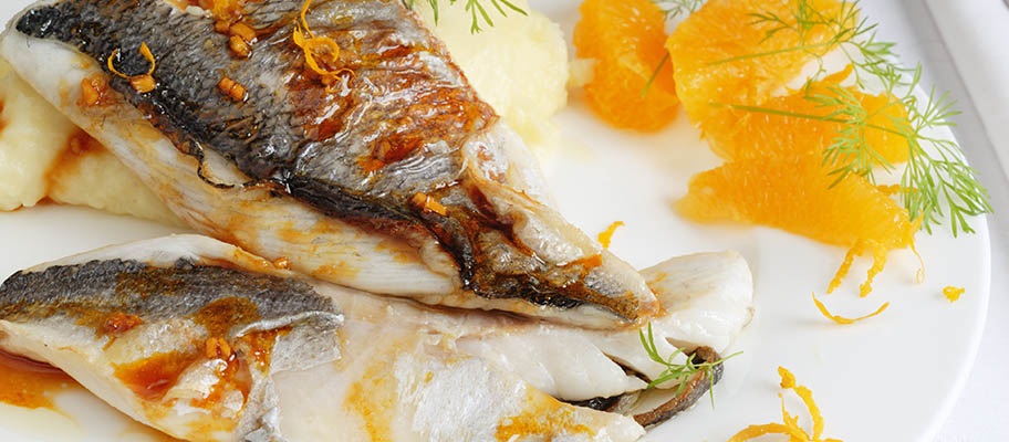 Hake fish fillets on white plate with saffron and pieces of mandarin orange