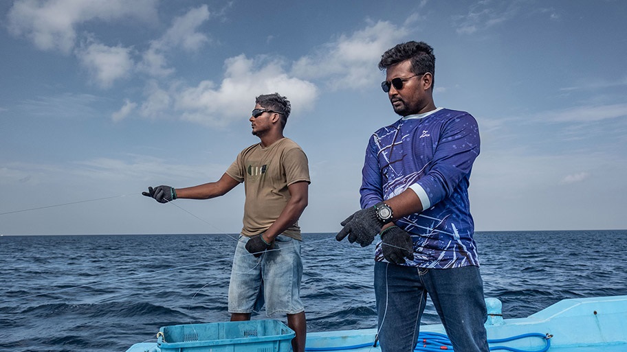 Two Maldives tuna fishers in sunglasses on boat holding fishing lines