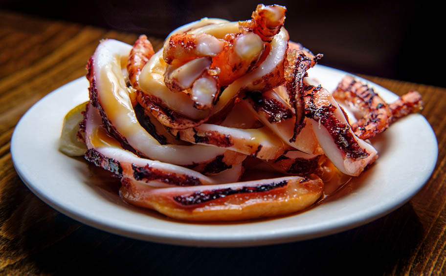 Grilled squid in sauce with lemon and tentacles on white plate