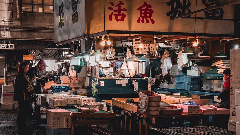 Two people standing at lit up Tokyo fish stall in dark early morning light