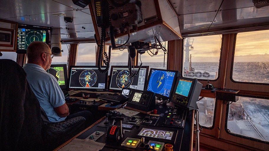 Fishing vessel cabin with captain sat in front of multiple screens
