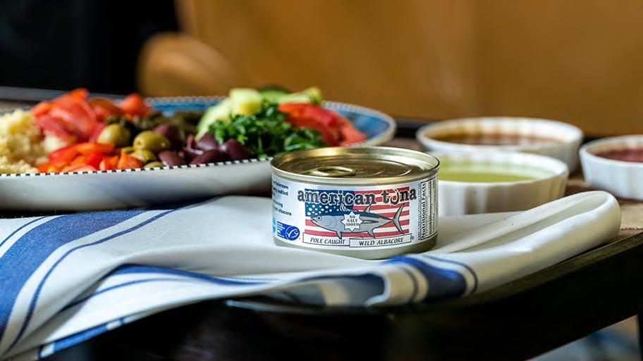 Tin / can of American brand albacore tuna on table cloth with plates of salad a dips behind