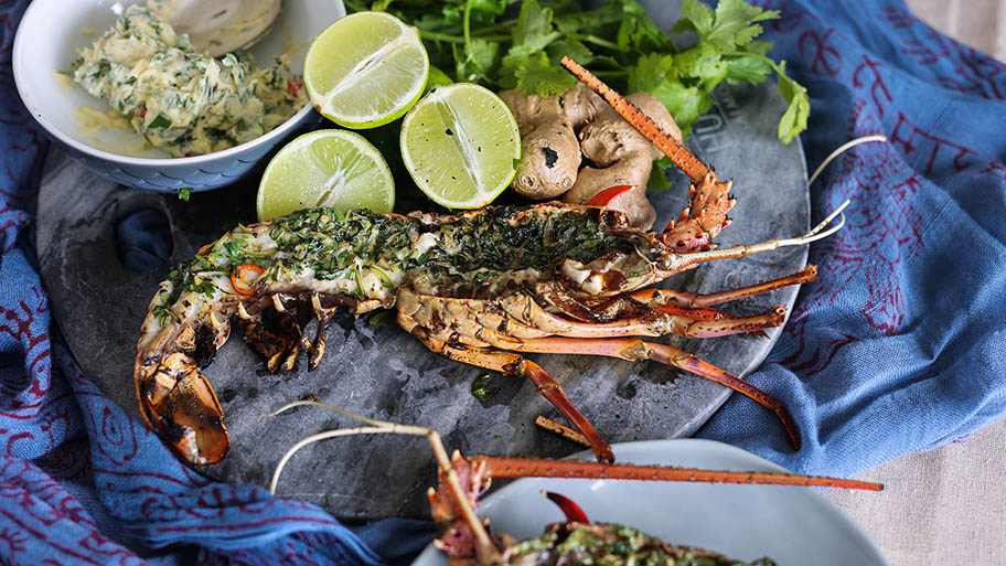 Grilled lobster on plate with lime, garnish and bowl of garlic butter