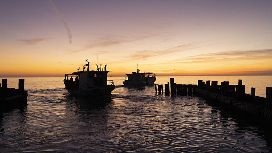 Sunset over water with two silhouetted fishing boats and wooden jetties