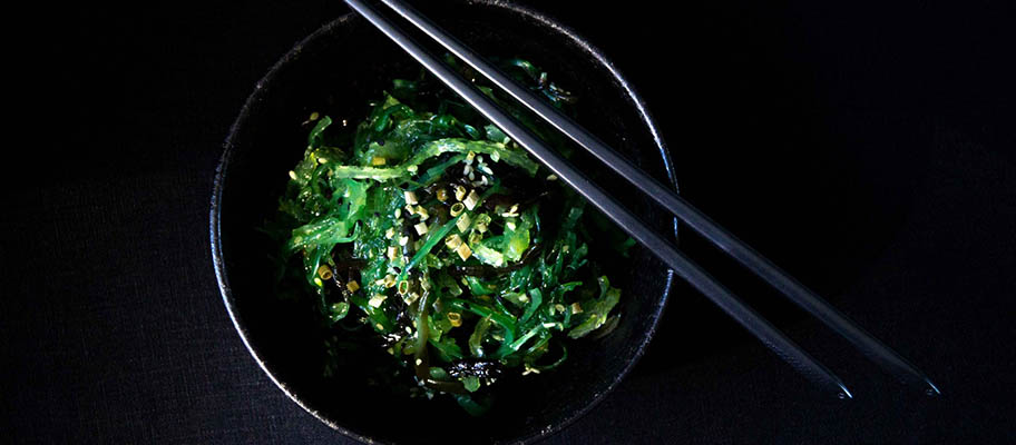 Aerial view of wakame seaweed in dark bowl with chopsticks laying across top