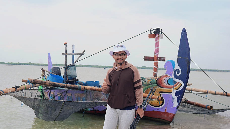 Student Research Grant recipient Jasiel Karosekali standing in front of small fishing boat