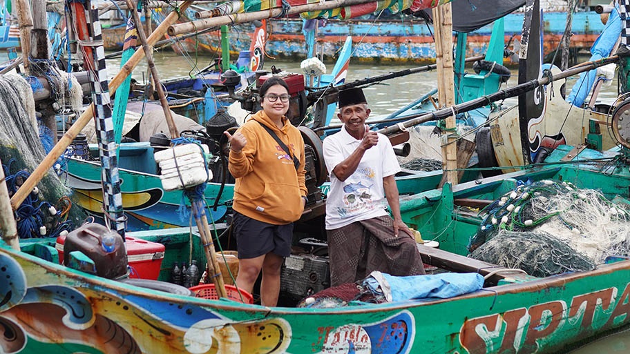Student Research Grant recipient Yefta Olivia Siahaan standing on colourful fishing boat with fisherman