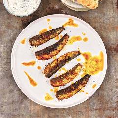Aerial view of grilled sardines on a white plate with splashes of sauce