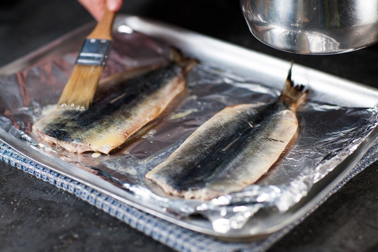 Oil being brushed on herring on a tray