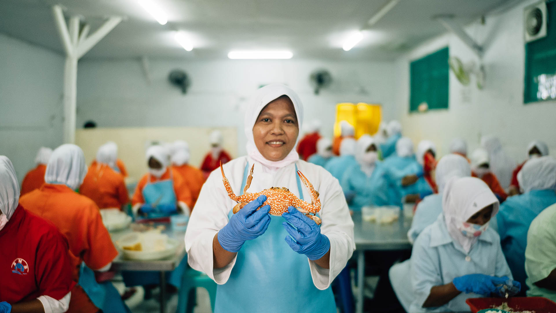 Woman wearing glasses and hijab passing  bucket of crabs to man with back to camera