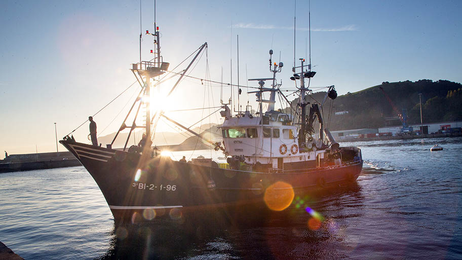 Fishing vessel in harbour against sunset with figure in silhouette on bow