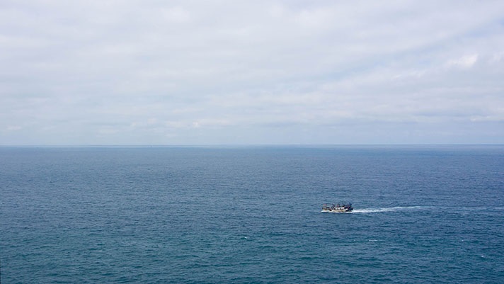 Traditional fishing boat in the sea seen from a distance with blue sea and sky