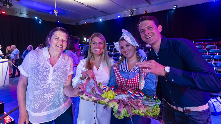 Four people celebrating Dutch new herring season, with one woman in traditional dress holding a tray of herring