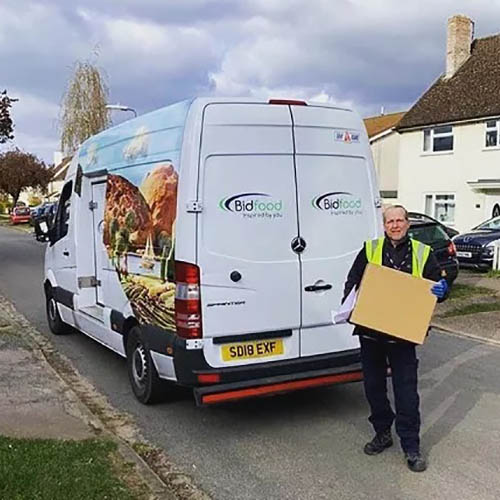 Bidfood delivery driver Man in hi-vis jacket holding a cardboard box by back doors of delivery van