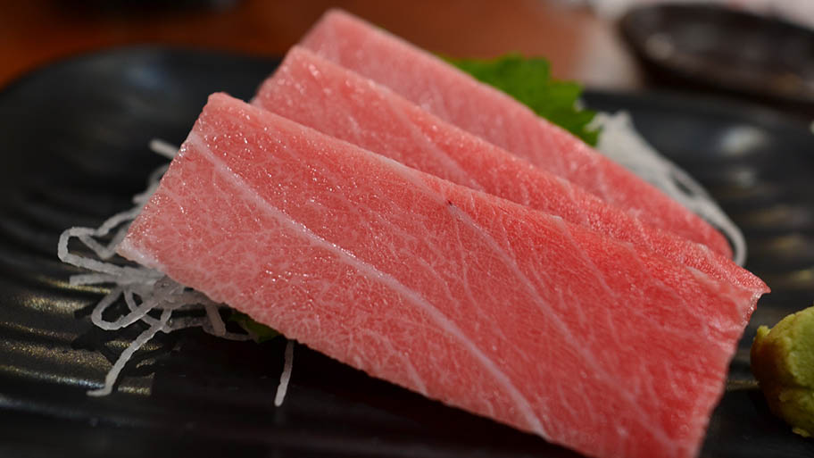 Three slices of tuna sashimi on dark plate with shredded daikon