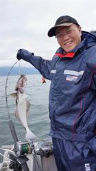 Main in waterproof clothes holding up a large fish on a line