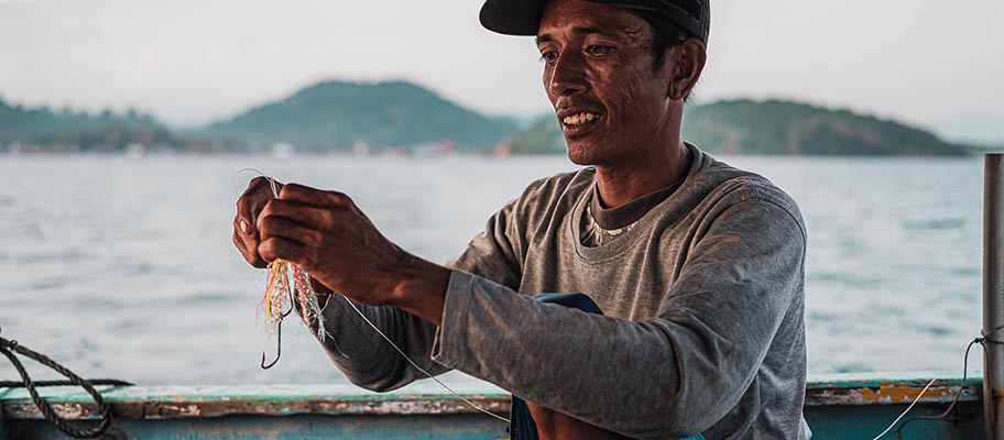 Man sitting on boat tying colurful bait to fishing hook