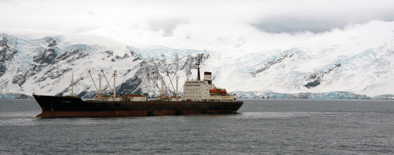 A krill boat floating in the sea in the Antarctic near snowy mountains.