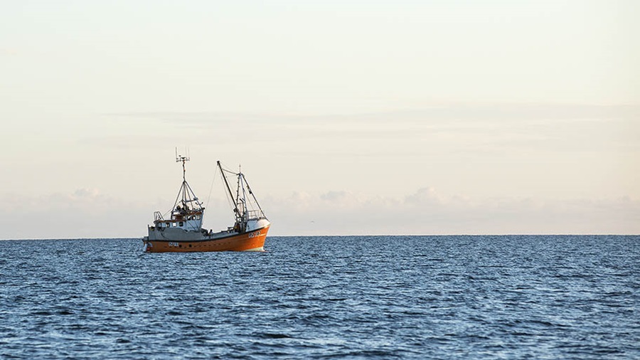 Medium sized boat on water, in middle distance against plain horizon