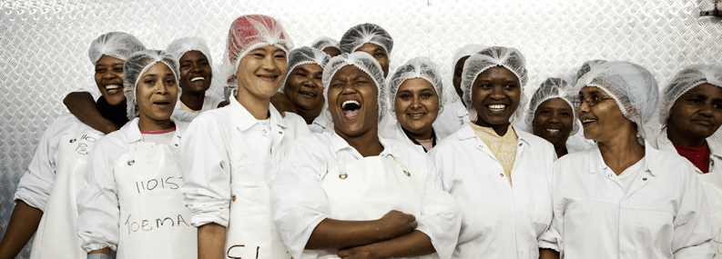 A group of individuals with hairnets and in white aprons laughing and smiling.