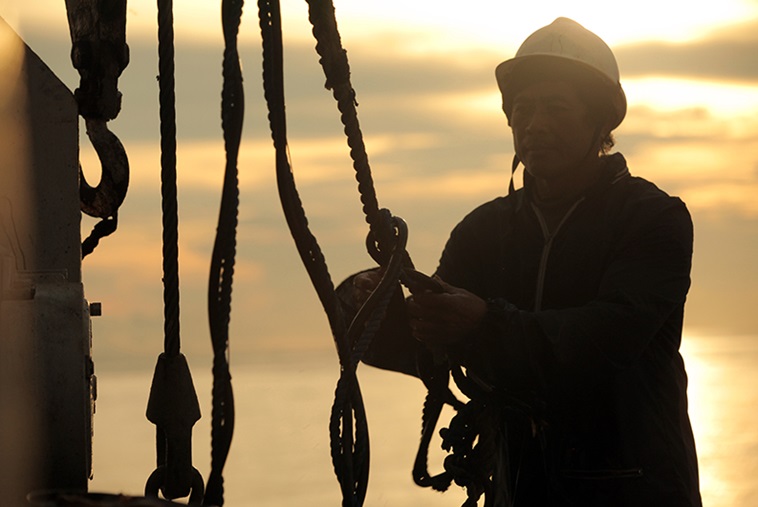 A sailor with a helmet adjusting ropes on a boat.
