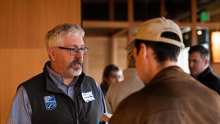 Main in bodywarmer with MSC logo talking to man in jacket and baseball cap