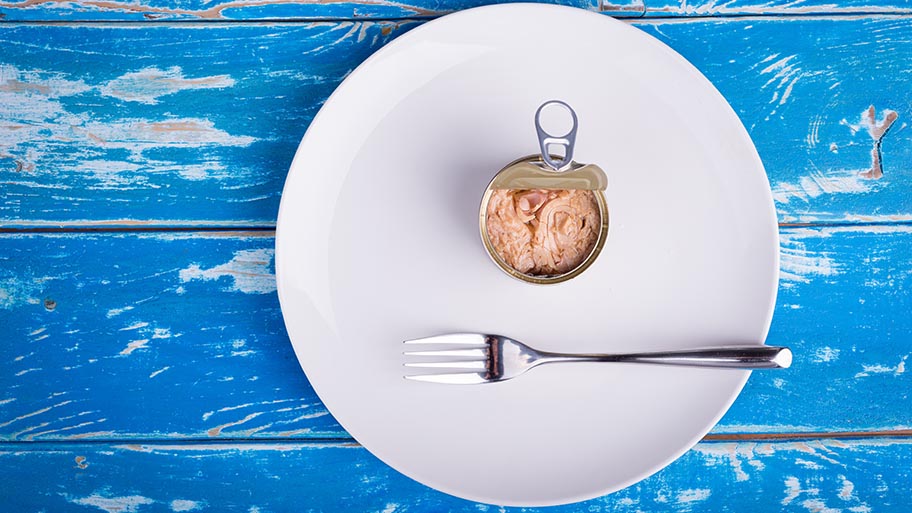Aerial shot of open can of tuna with fork on white plate on blue wooden table