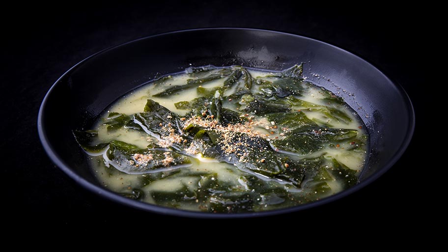 Seaweed soup with spice garnish in dark bowl