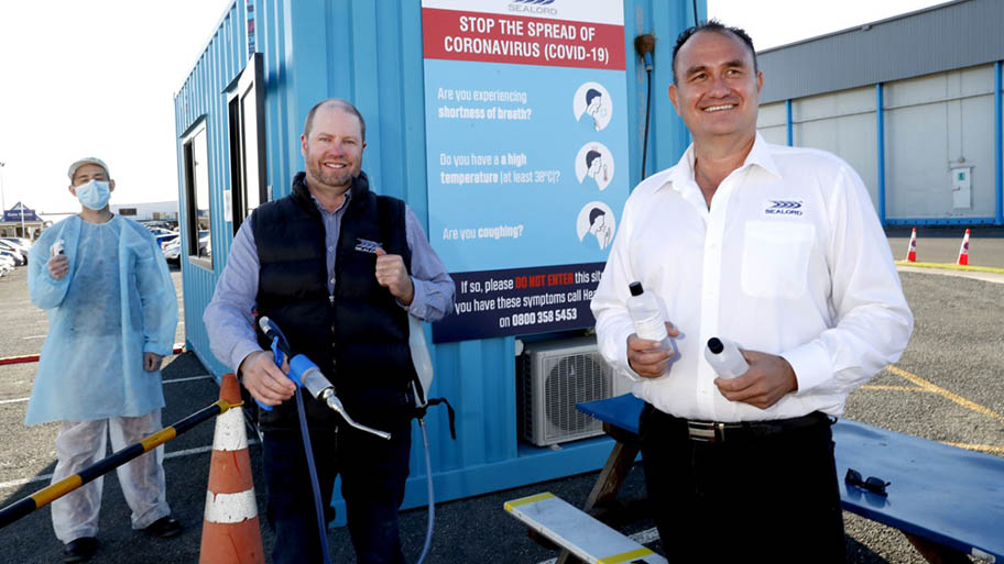 Three men outside portacabin with sanitising equipment