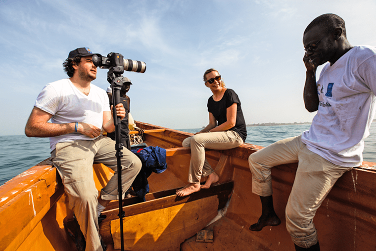 Three people on a boat in Gambia, one with a camera.